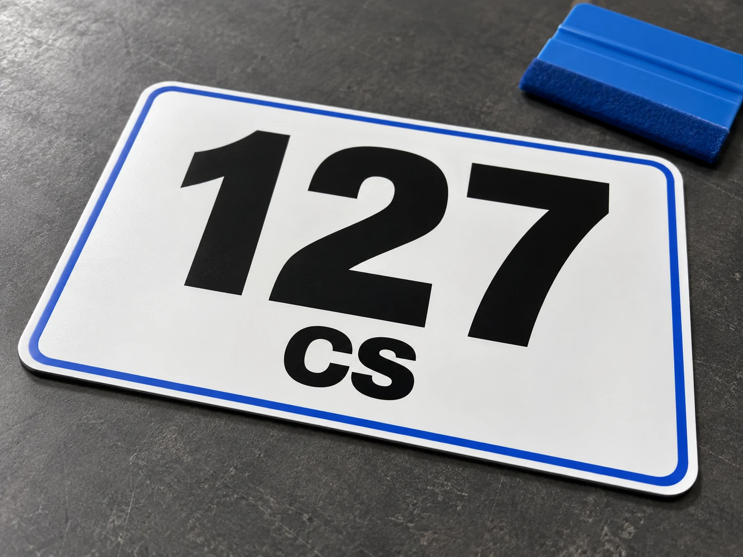 Generated concept of a white 127 CS number panel with rounded corners and a blue border on a workbench